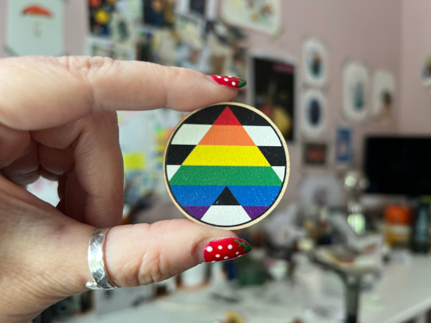 A close up of a wooden 4cm dia round pin with the Pride ally flag on