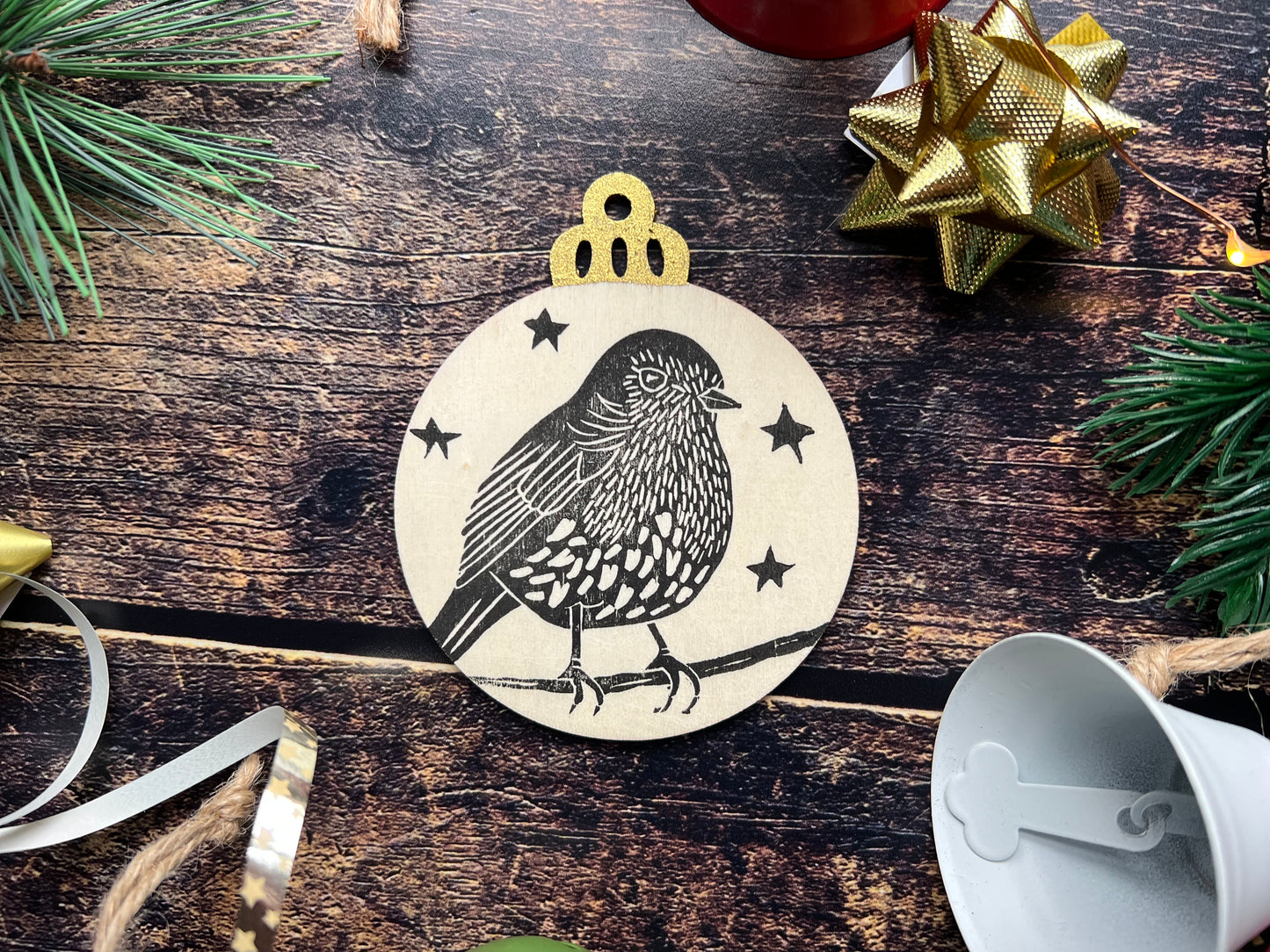 A wooden handprinted flat baubel depicting a robin on a branch