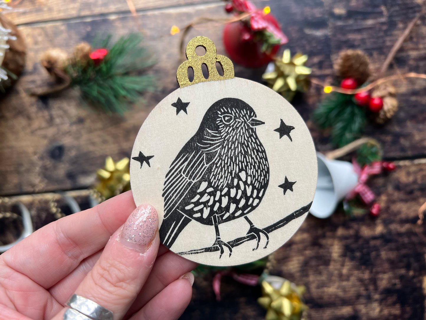 A wooden handprinted flat baubel depicting a robin on a branch