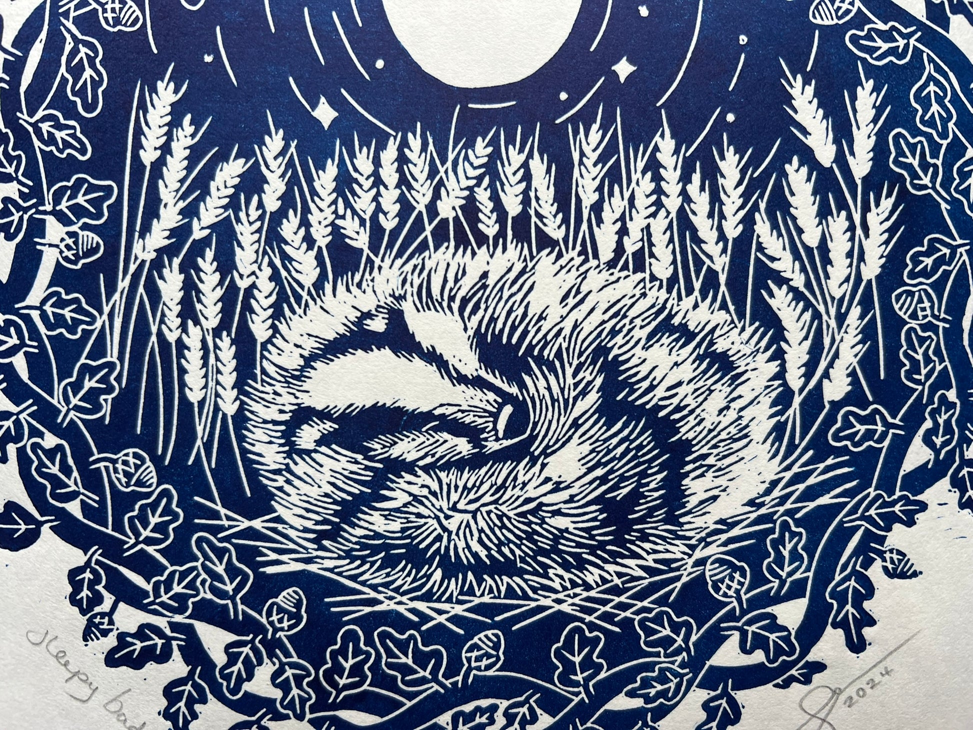 A handprinted linoprint of a badger sleeping in a field of wheat.