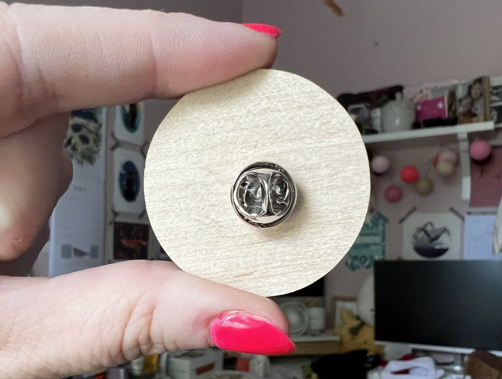 The back of a 4cm dia round wooden pin with a metal butterfly fastener